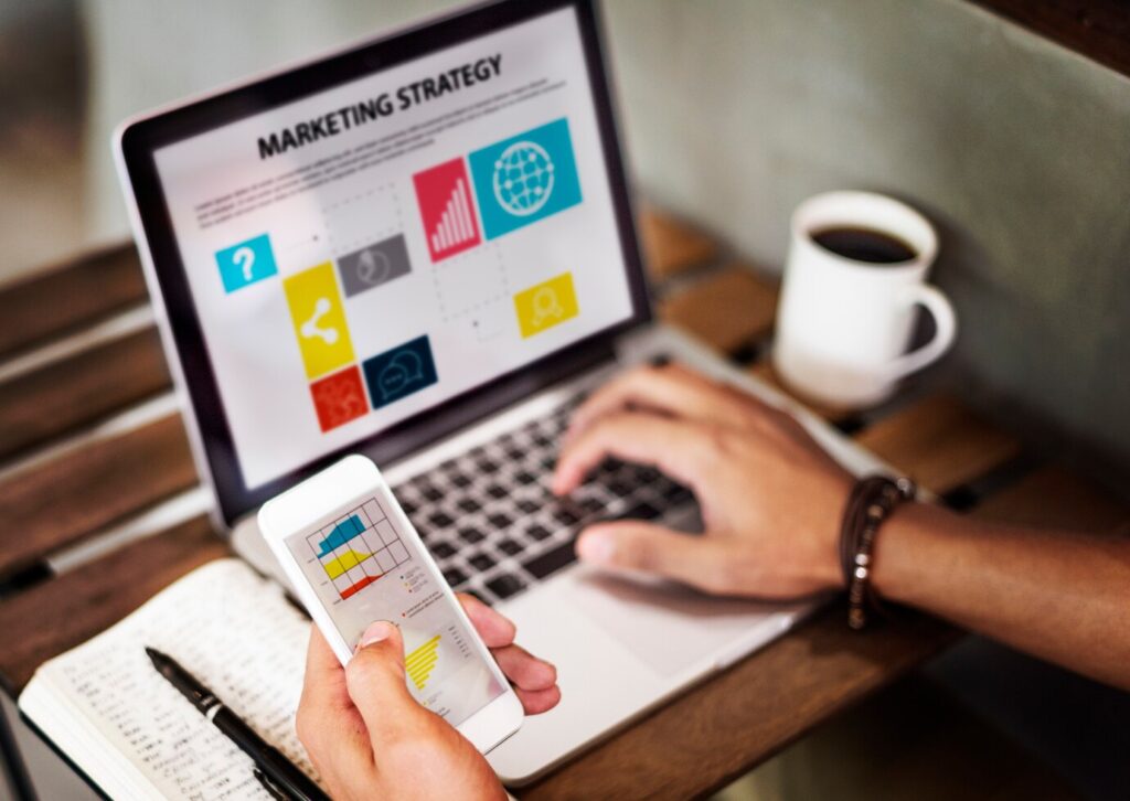 Person analyzing marketing strategy on laptop and phone, related to digital marketing services Islamabad.